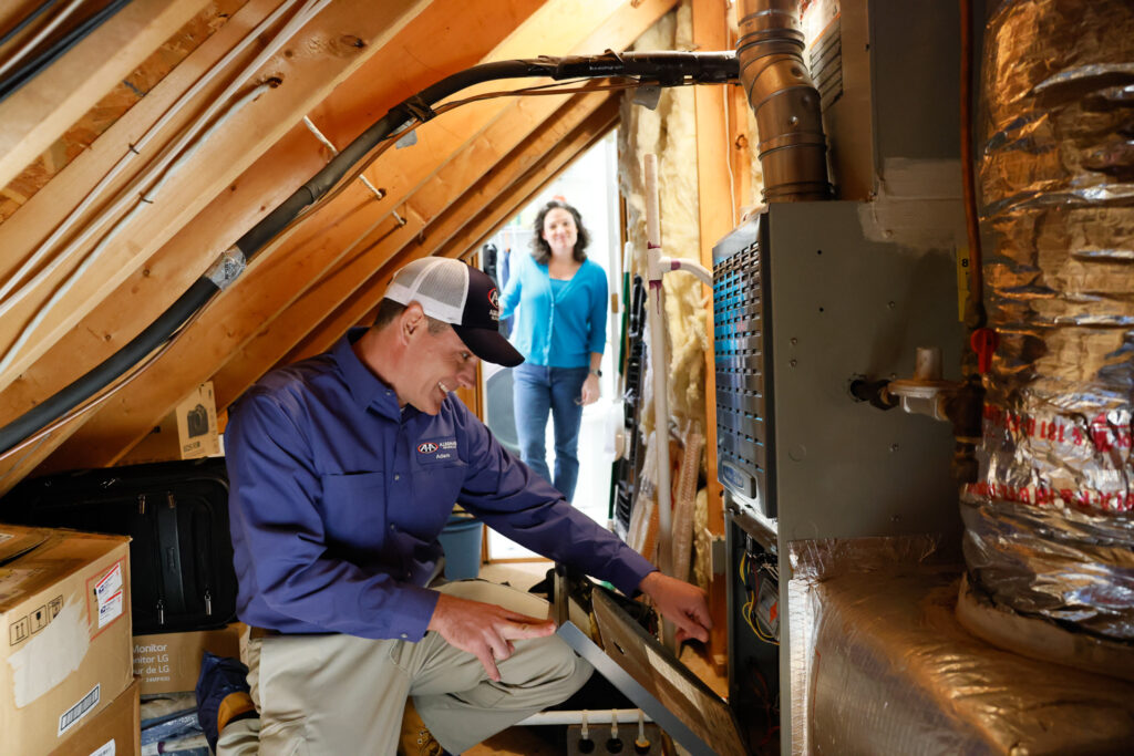 Technician servicing a gas furnace in an unfinished attic.