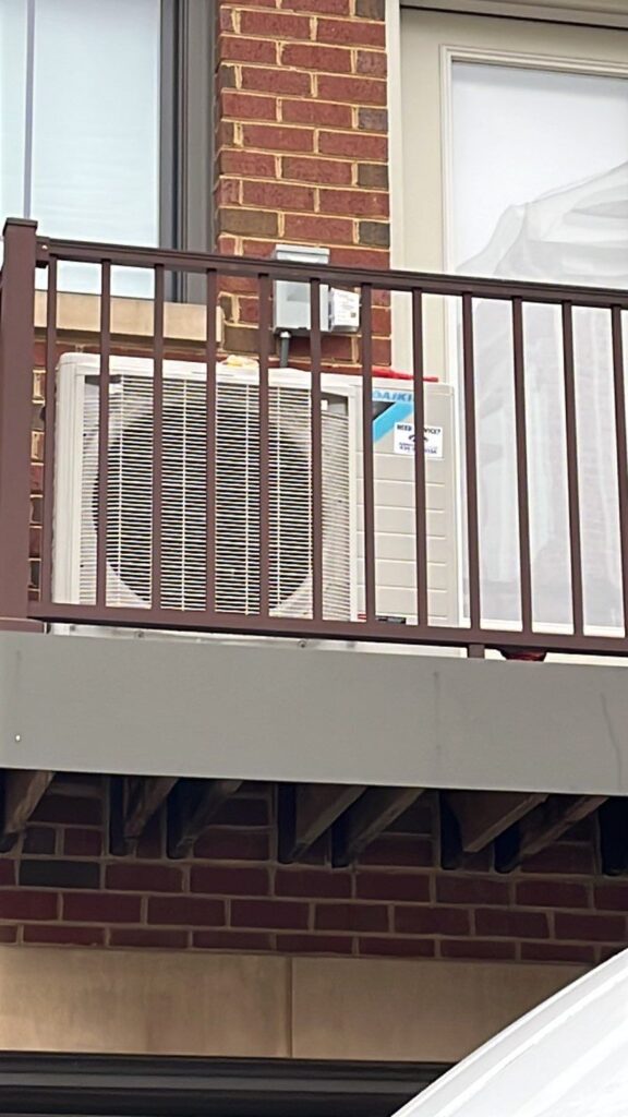 View from street of a new Daikin Fit heat pump on townhome deck
